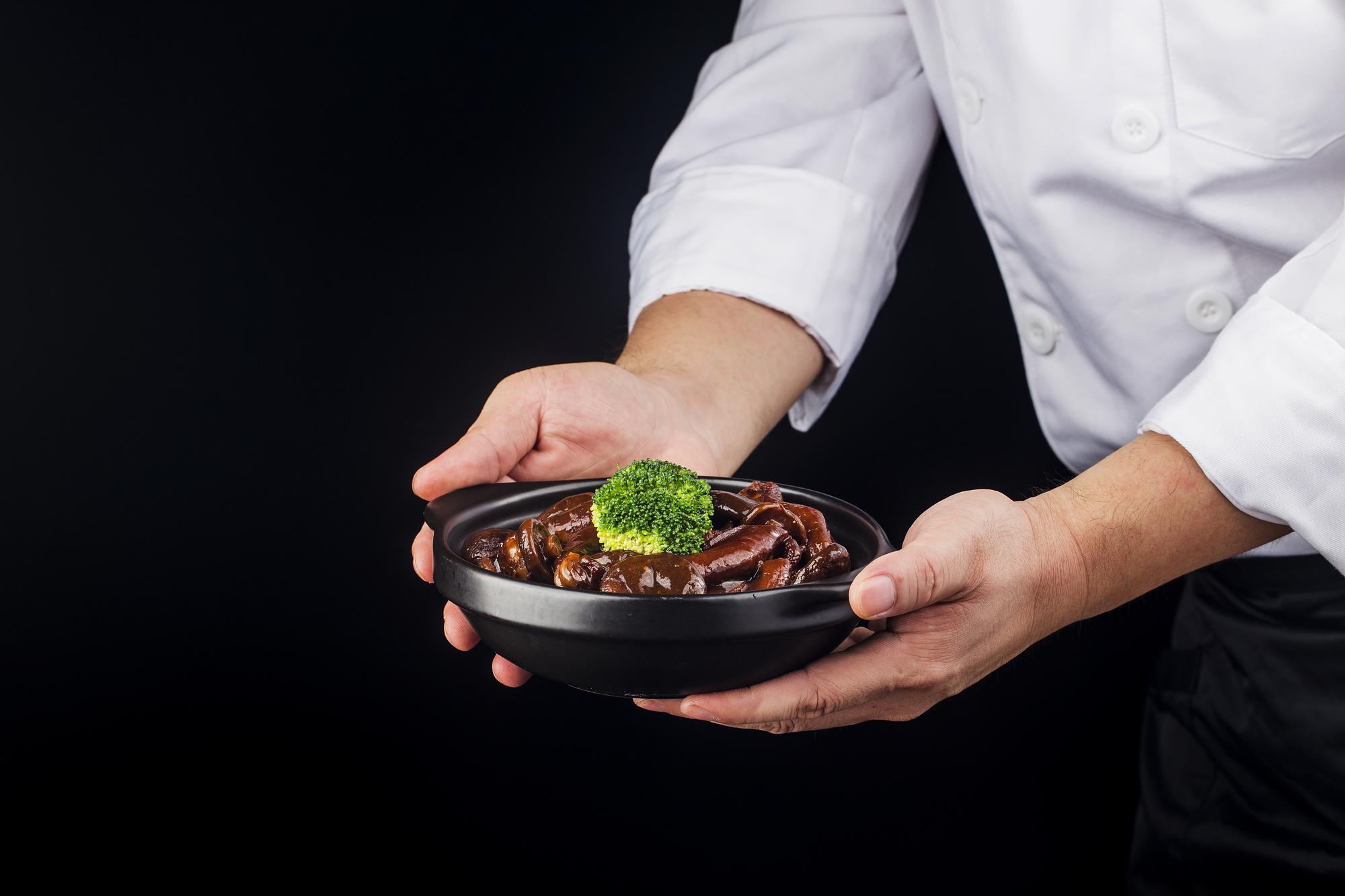 Chef presenting a plated modern dish on a dark tabletop